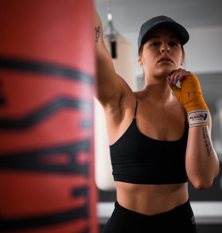 women in black sports bra and orange boxing wraps wraps hitting red punching bag