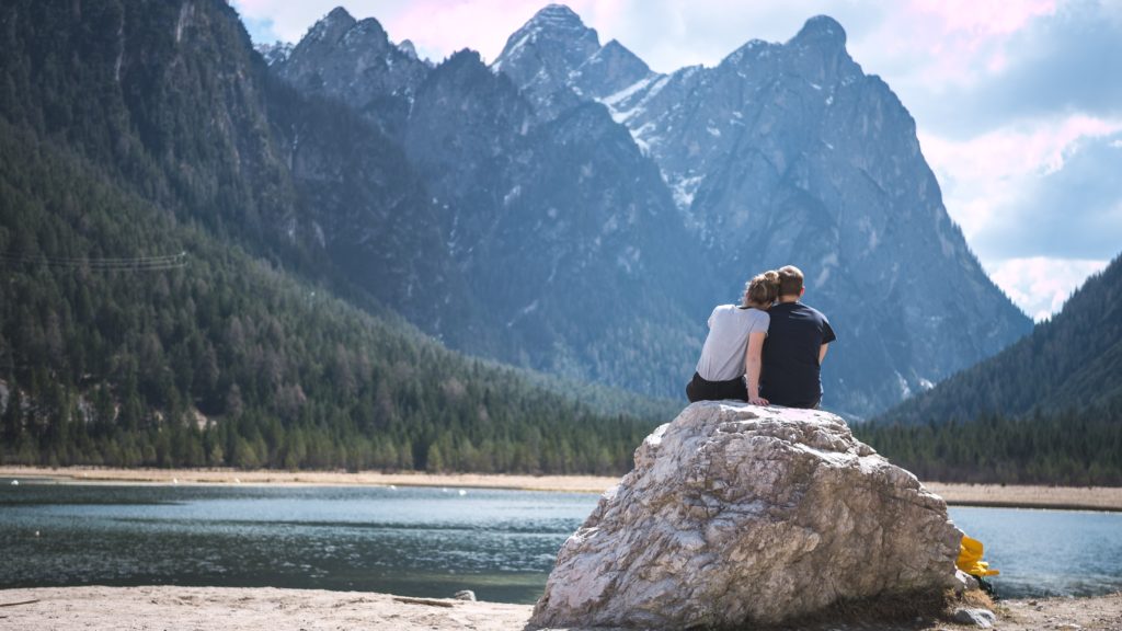 couple sat on rock looking out to a river, forest and mountains