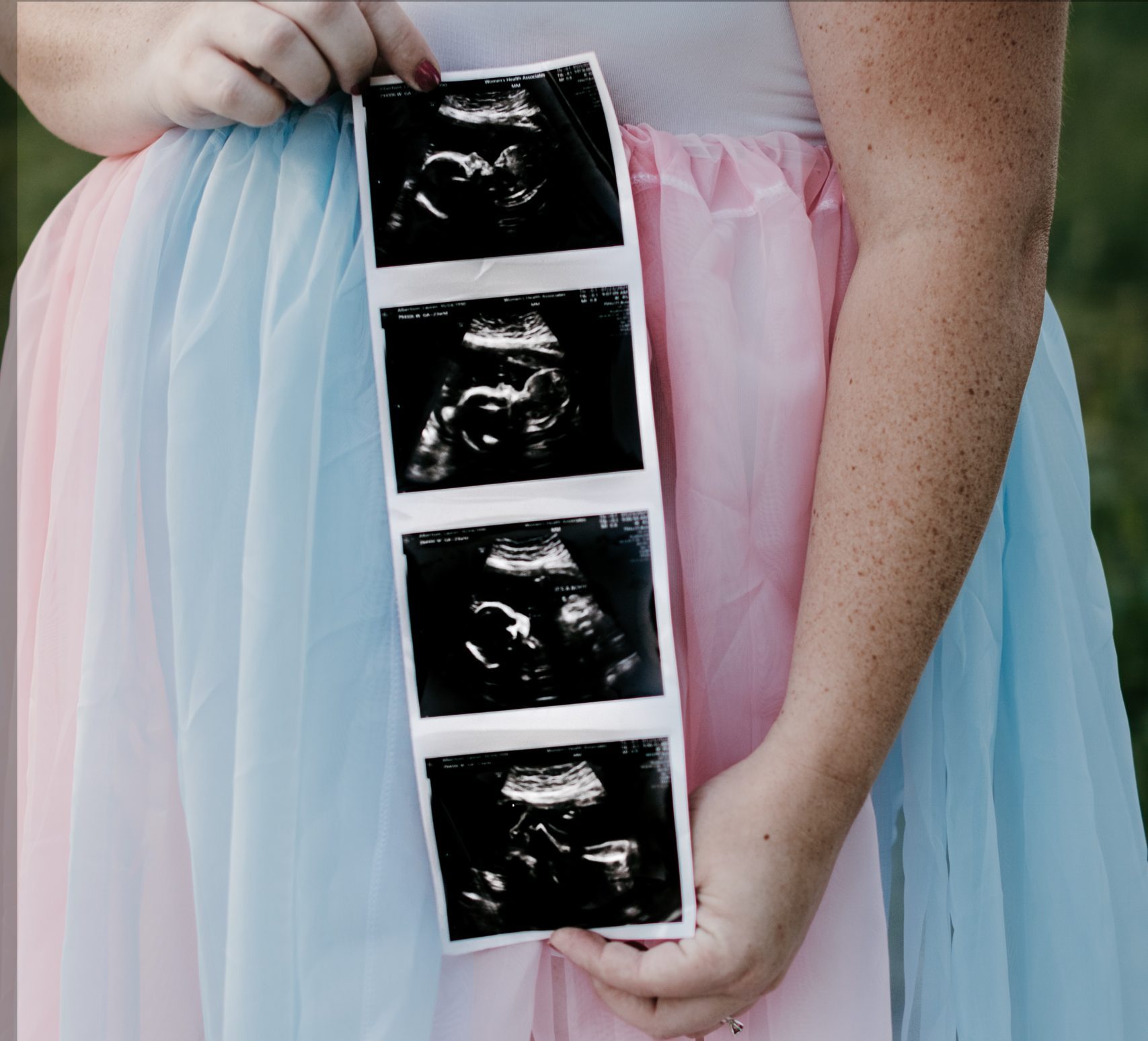 woman holding ultrasound images in front of pregnant belly