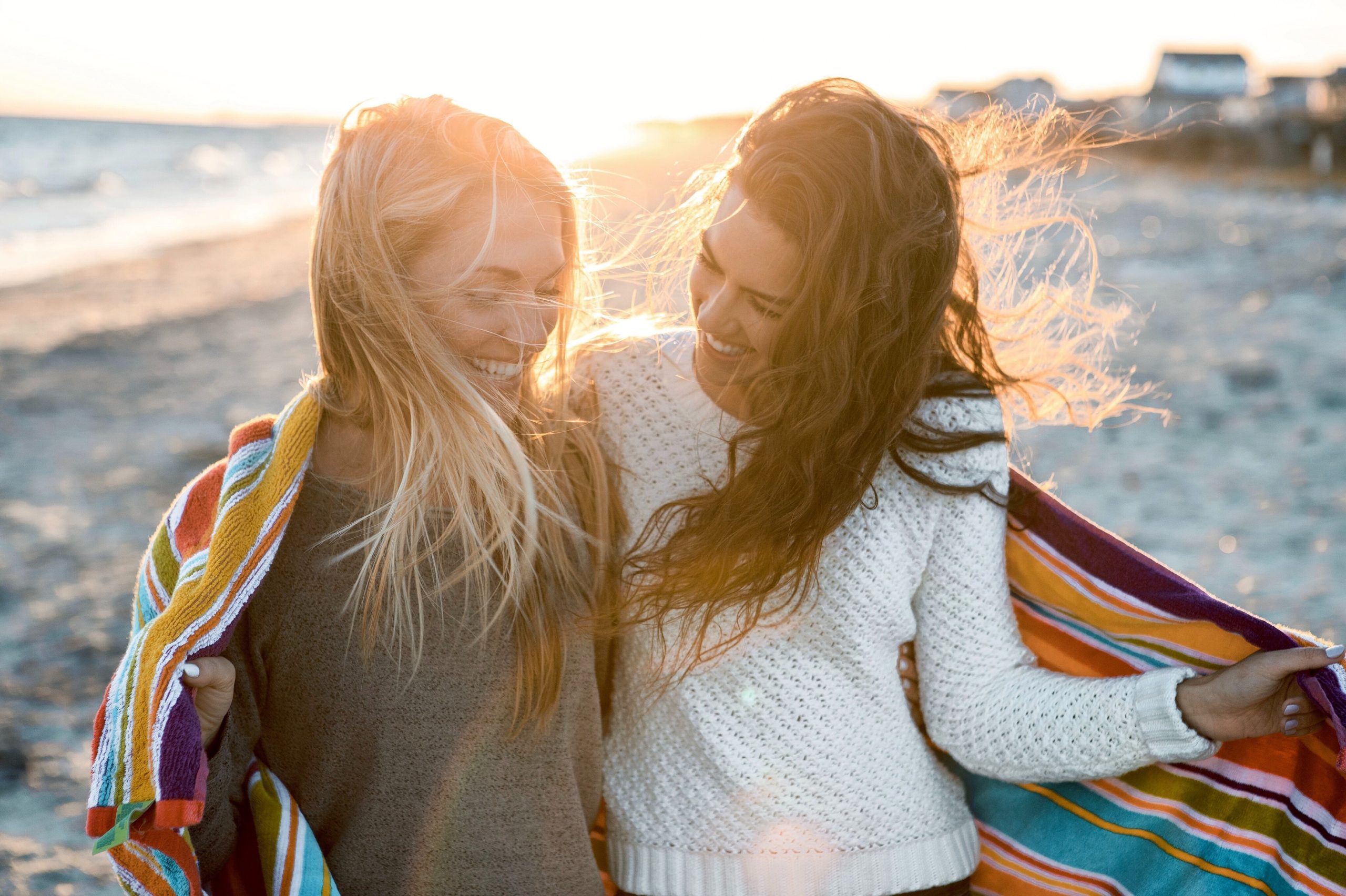 Two female friends on the beach with a blanket around them