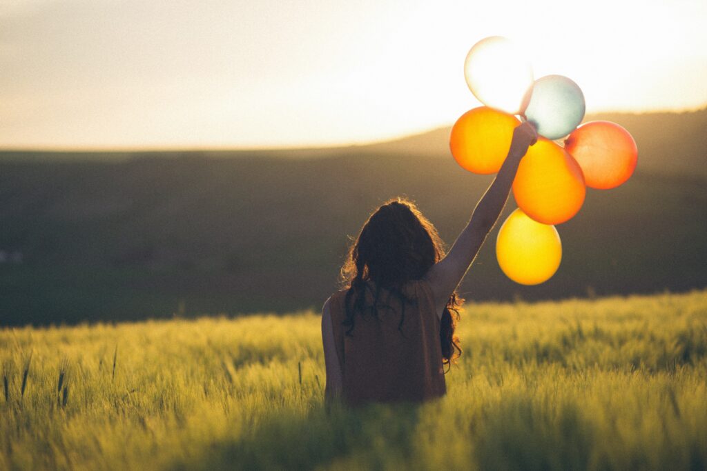 Woman appreciating life sat in grass holding a bunch of balloons